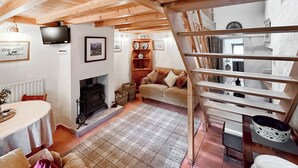 A cozy living room with a fireplace, a sofa, a dining table, and a staircase.