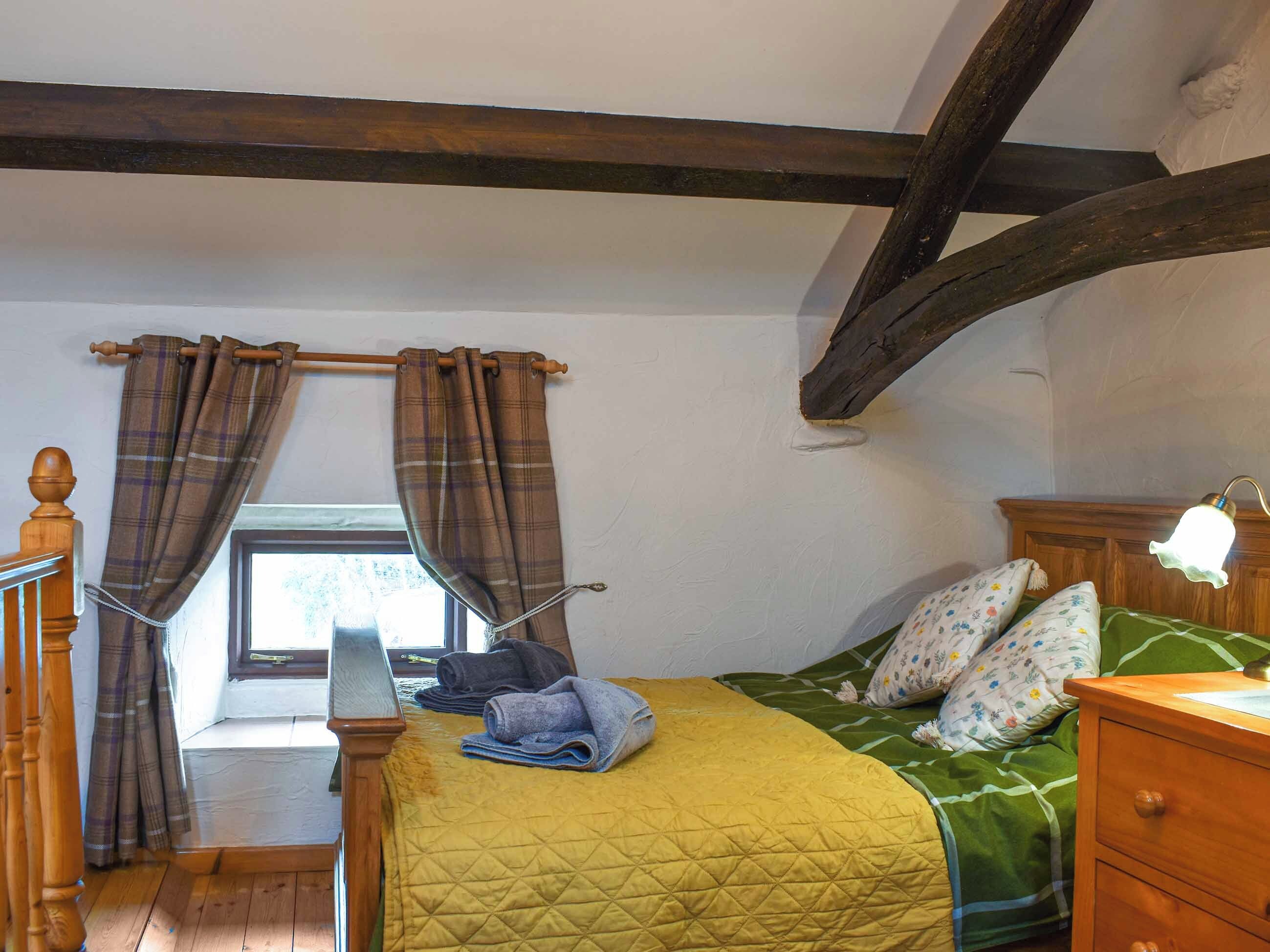 Une chambre à coucher avec un lit, une table de chevet, une fenêtre avec des rideaux et une poutre en bois au plafond.