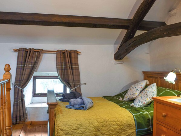 Une chambre à coucher avec un lit, une table de chevet, une fenêtre avec des rideaux et une poutre en bois au plafond.
