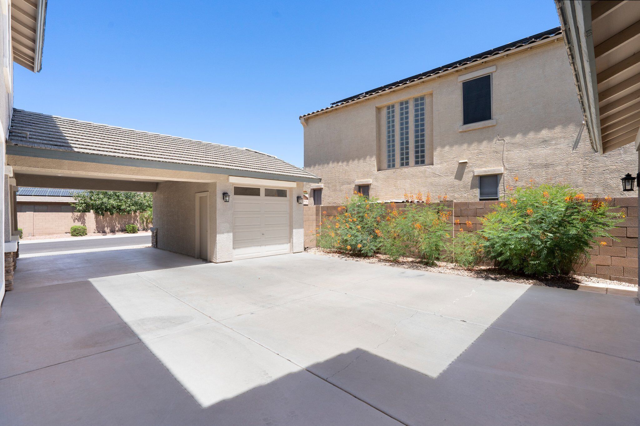A residential property with a covered driveway, a garage, and a brick wall with flowering plants.