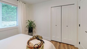 Ein Schlafzimmer mit einem großen Bett, einem Fenster mit Jalousien, einem Blumentopf und einem Kleiderschrank.