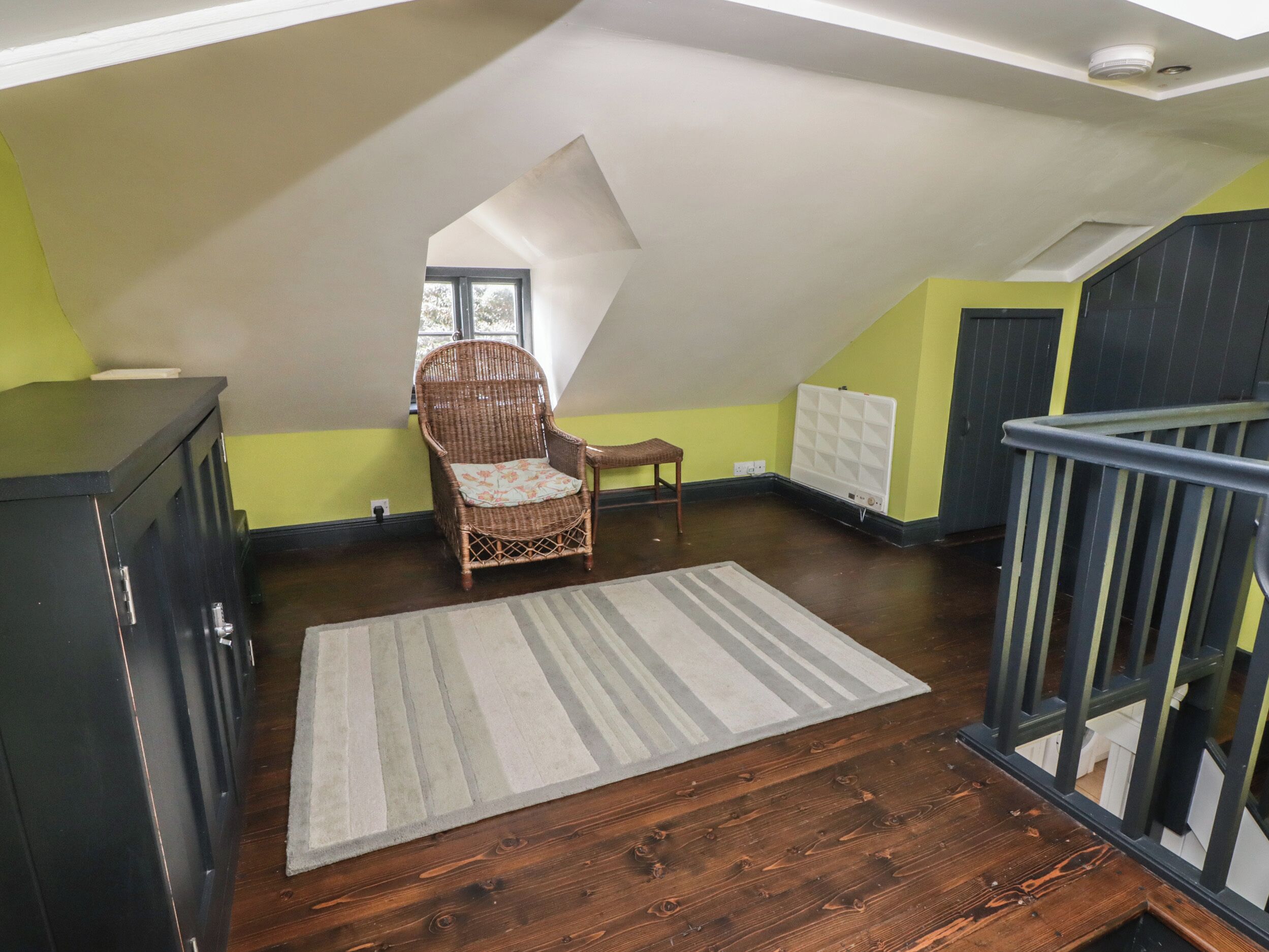A room with a sloped ceiling, a wicker chair, a striped rug, and a radiator.