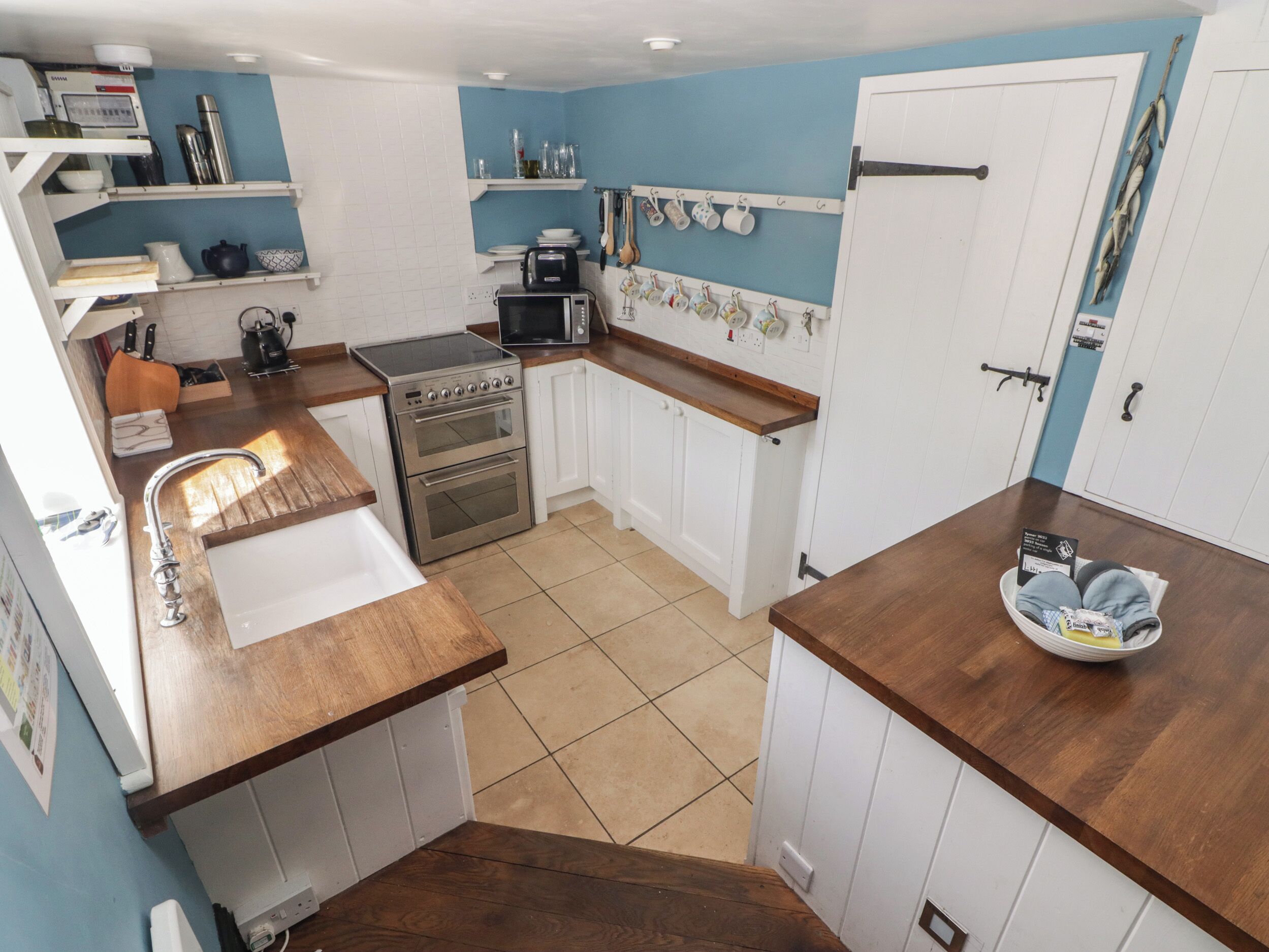 Una cocina compacta con muebles blancos, un horno de acero inoxidable, un microondas y un lavamanos.