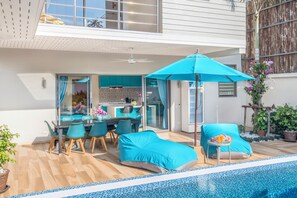 Ett modernt utomhusområde med pool, en möblerad, skyddad sittplats och en matplats.