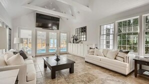 A spacious living room with a white sofa, a coffee table, and a view of a pool through glass doors. - Heated Indoor Pool and Spa - Golf Course View (Mashpee)