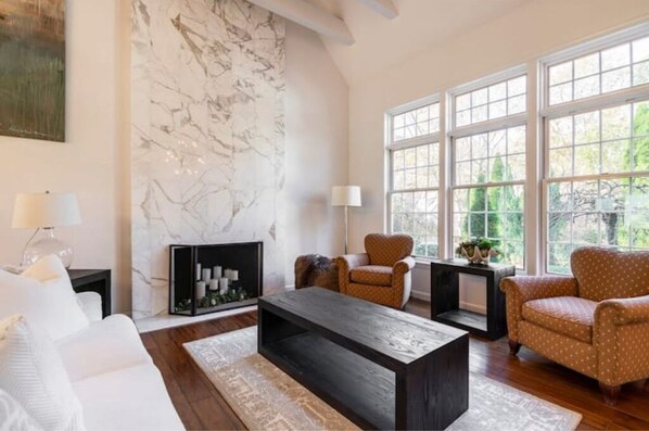 A living room with a fireplace, large windows, and a marble wall. - Heated Indoor Pool and Spa - Golf Course View (Mashpee)