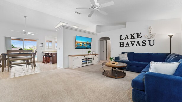 A spacious living room with a blue couch, a coffee table, and a TV mounted on the wall. - STOCKED Pool Home, RV & Boat parking, Game room. Sleeps 13 (Lake Havasu City)