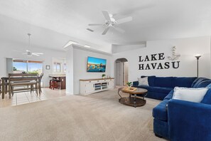 A spacious living room with a blue couch, a coffee table, and a TV mounted on the wall. - STOCKED Pool Home, RV & Boat parking, Game room. Sleeps 13 (Lake Havasu City)