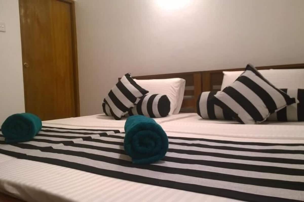 A hotel room with a striped bedspread, two teal rolled towels, and black and white striped pillows.