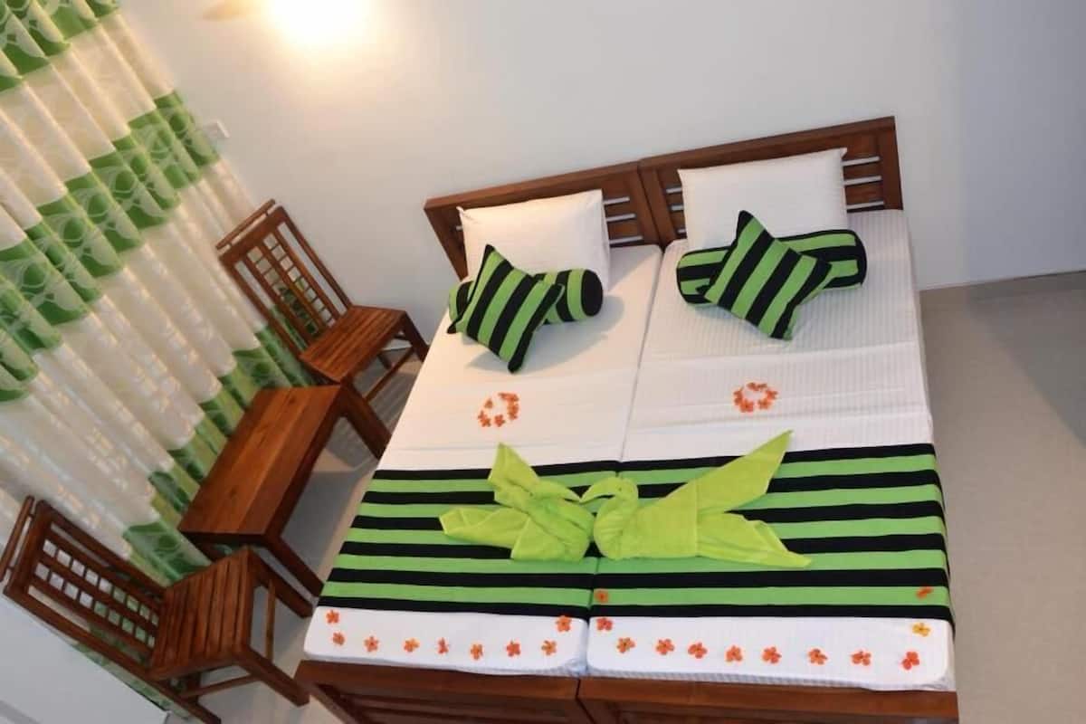 A neatly made bed with striped bedding and floral pillows, a wooden chair, and a table with a green cloth.