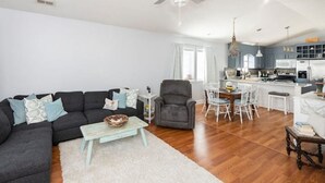 Un salon moderne avec un canapé foncé, une table basse et un coin repas comprenant une table et des chaises blanches.
