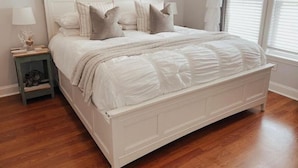 Un lit blanc avec une couette matelassée, une table de chevet avec une lampe et une fenêtre avec des stores.