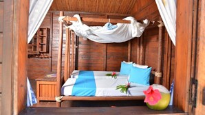 Una habitación de madera con una cama bajo un dosel, una mesita y una planta decorativa.