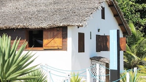 A traditional thatched-roof house with a white exterior and wooden shutters, surrounded by a rope barrier and tropical plants. - Comfort Villa with Sea View (Sainte-Marie)