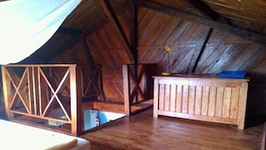 A rustic attic room with wooden beams, a bed, a small table, and a window with a white curtain. - Comfort Villa with Sea View (Sainte-Marie)