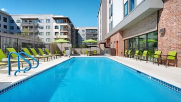 Una piscina con sillas de descanso y sombrillas, rodeada de edificios modernos.