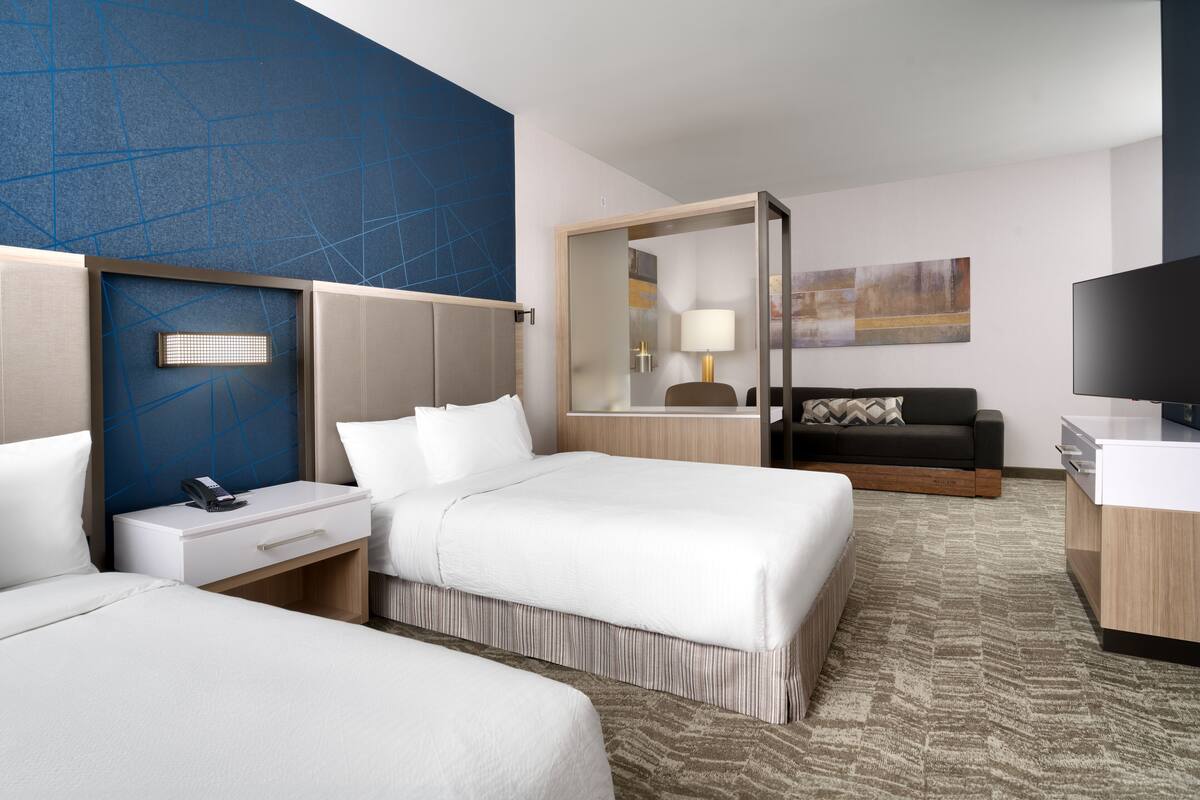 A hotel room with two beds, a sofa, a TV, and a desk.