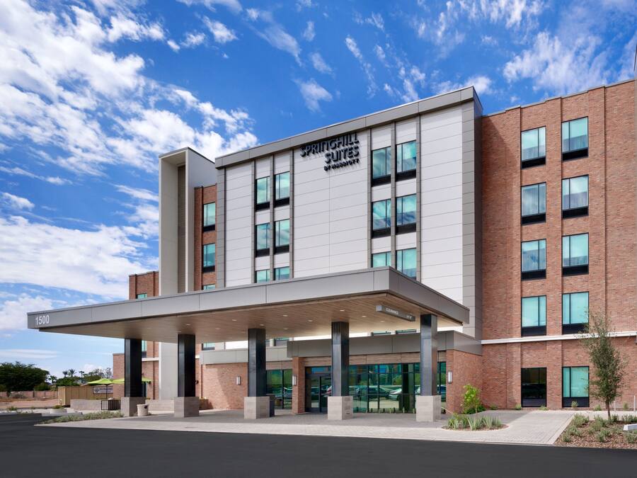 A modern hotel with a covered entrance, multiple floors, and a clear sky.