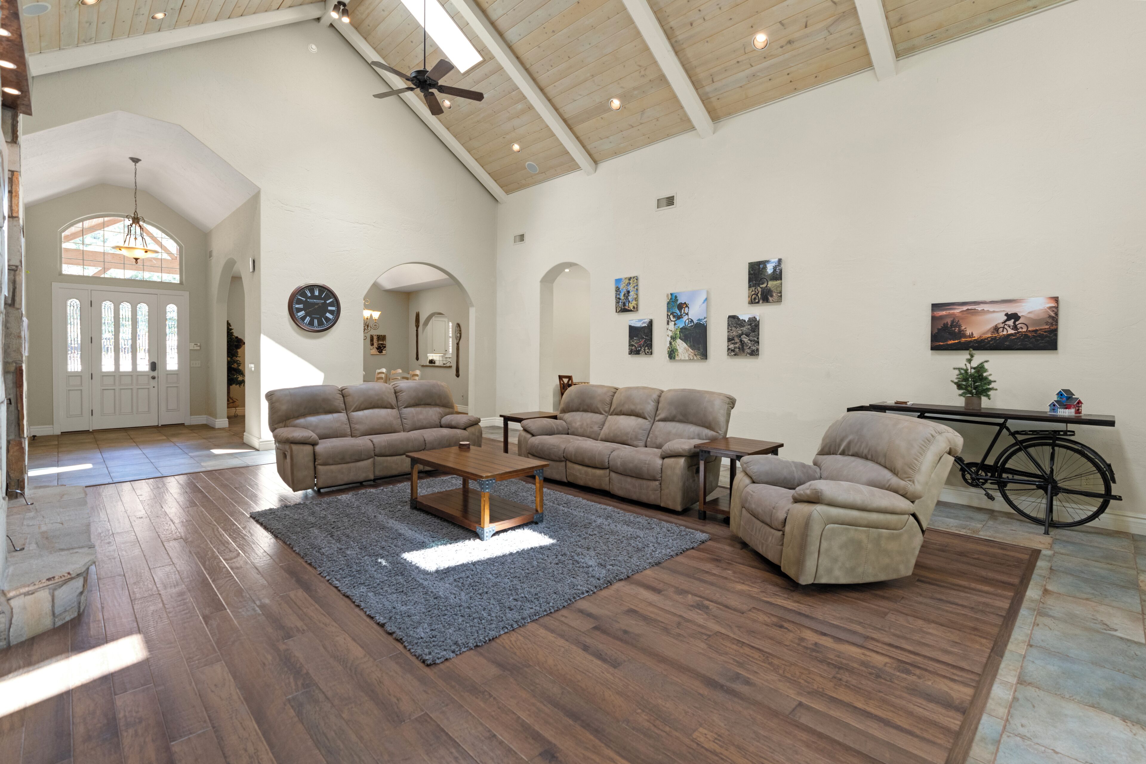 A spacious living room with a wooden ceiling, a large sofa set, a coffee table, and a bicycle in the corner.