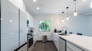 A modern kitchen with white cabinets, a stainless steel oven, a sink, and pendant lights. - Hotel Mai Downtown Long Beach (Long Beach)