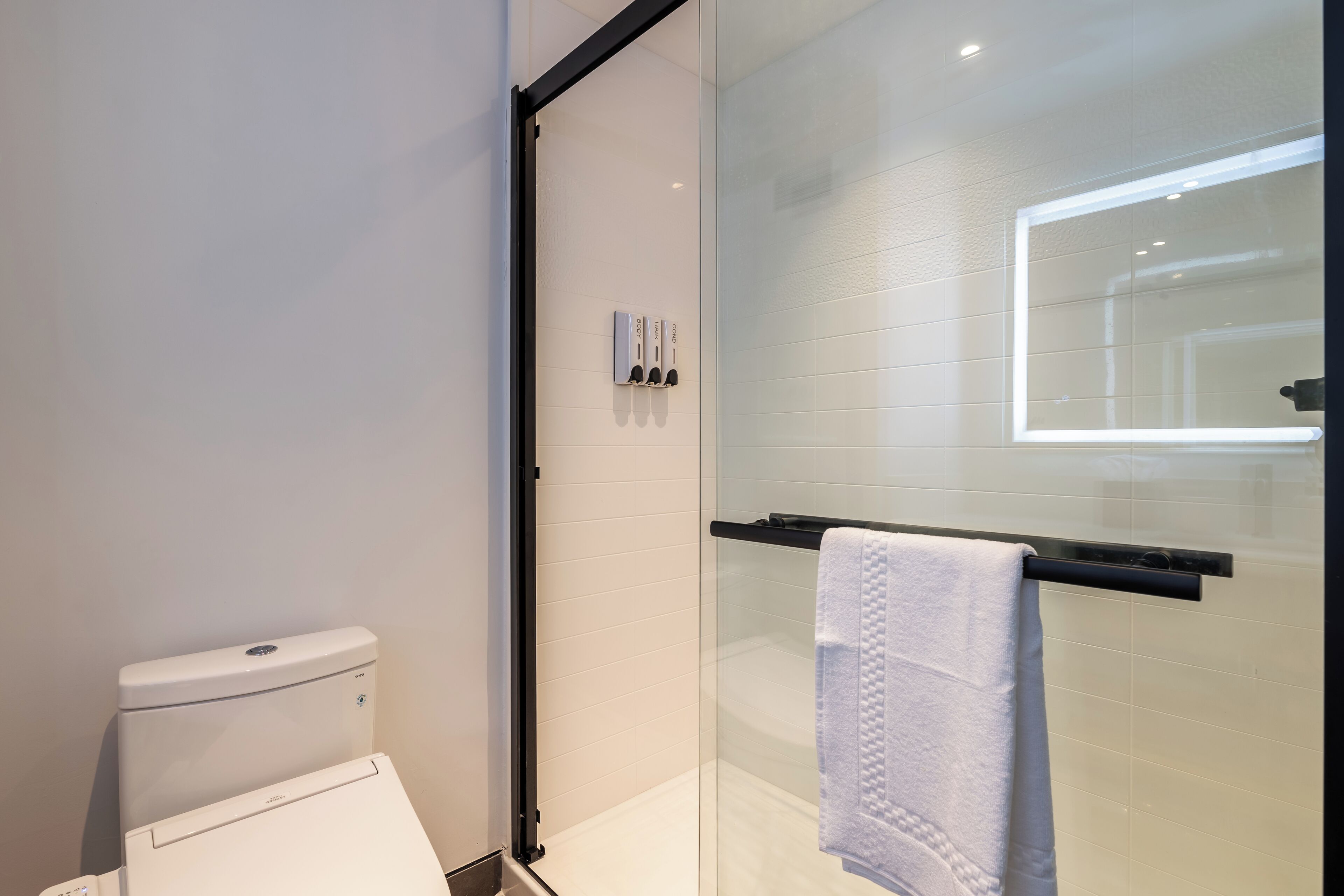 Un baño moderno con cabina de ducha de vidrio, inodoro blanco y toallero con una toalla blanca.