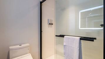 Un baño moderno con cabina de ducha de vidrio, inodoro blanco y toallero con una toalla blanca.