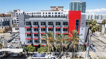 A modern building with multiple floors, balconies, and a parking area with cars and a bus.