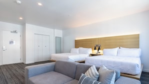 A hotel room with two beds, a sofa, and a nightstand with a lamp. - Hotel Mai Downtown Long Beach (Long Beach)