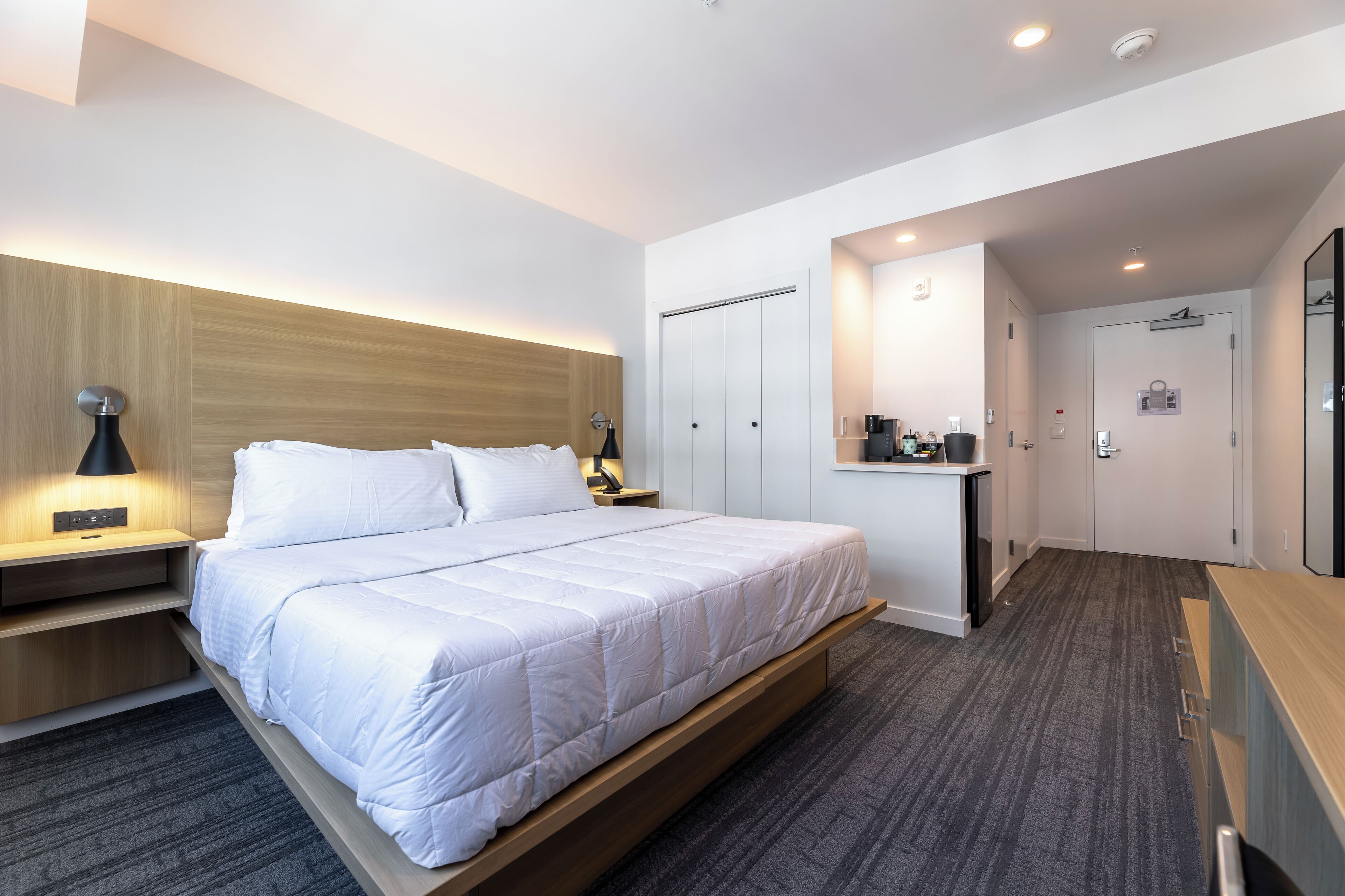 A modern hotel room with a large bed, bedside tables, a desk, and a wardrobe.
