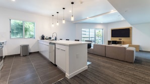 A modern kitchen with a central island, a dining area with a sofa, and a flat-screen TV mounted on the wall. - Hotel Mai Downtown Long Beach (Long Beach)