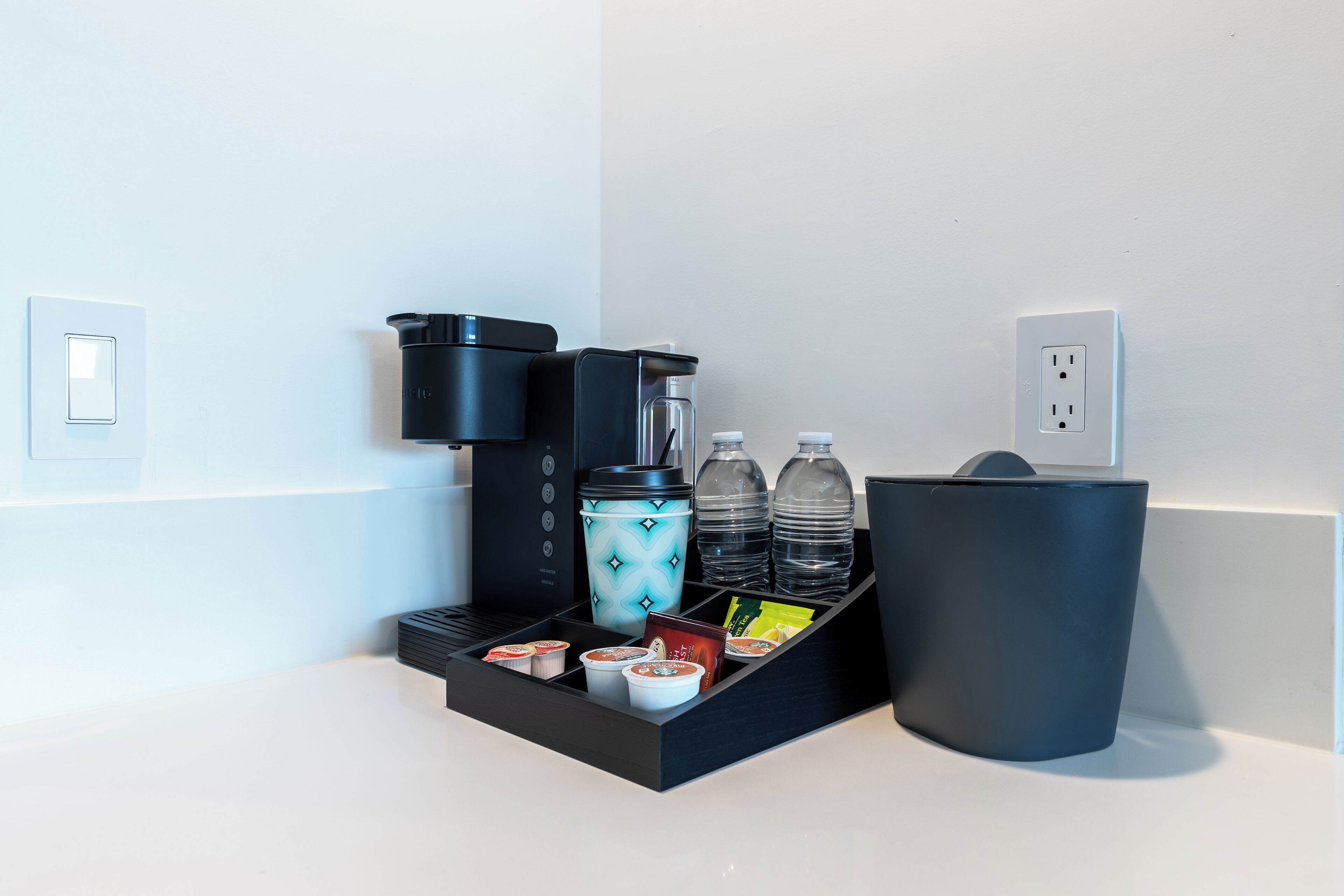 A coffee station with a coffee maker, cups, and a water dispenser.