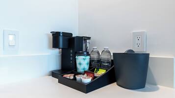 A coffee station with a coffee maker, cups, and a water dispenser.