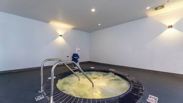 Un jacuzzi con barandas de metal, rodeado de un piso de baldosas, con un panel de control y una lámpara fijada a la pared.