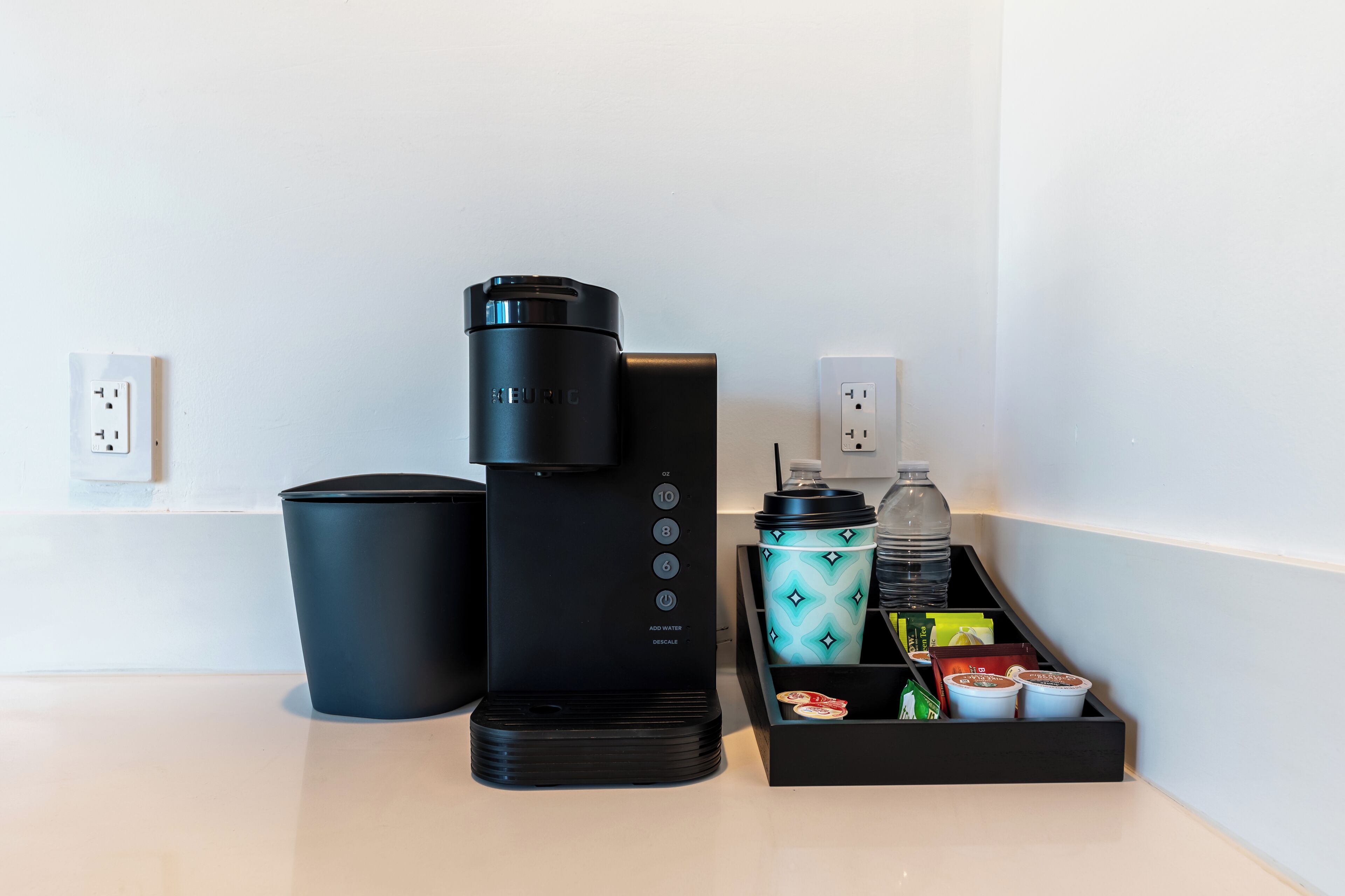 Uma cafeteira, uma lixeira e uma garrafa de água em uma bancada.