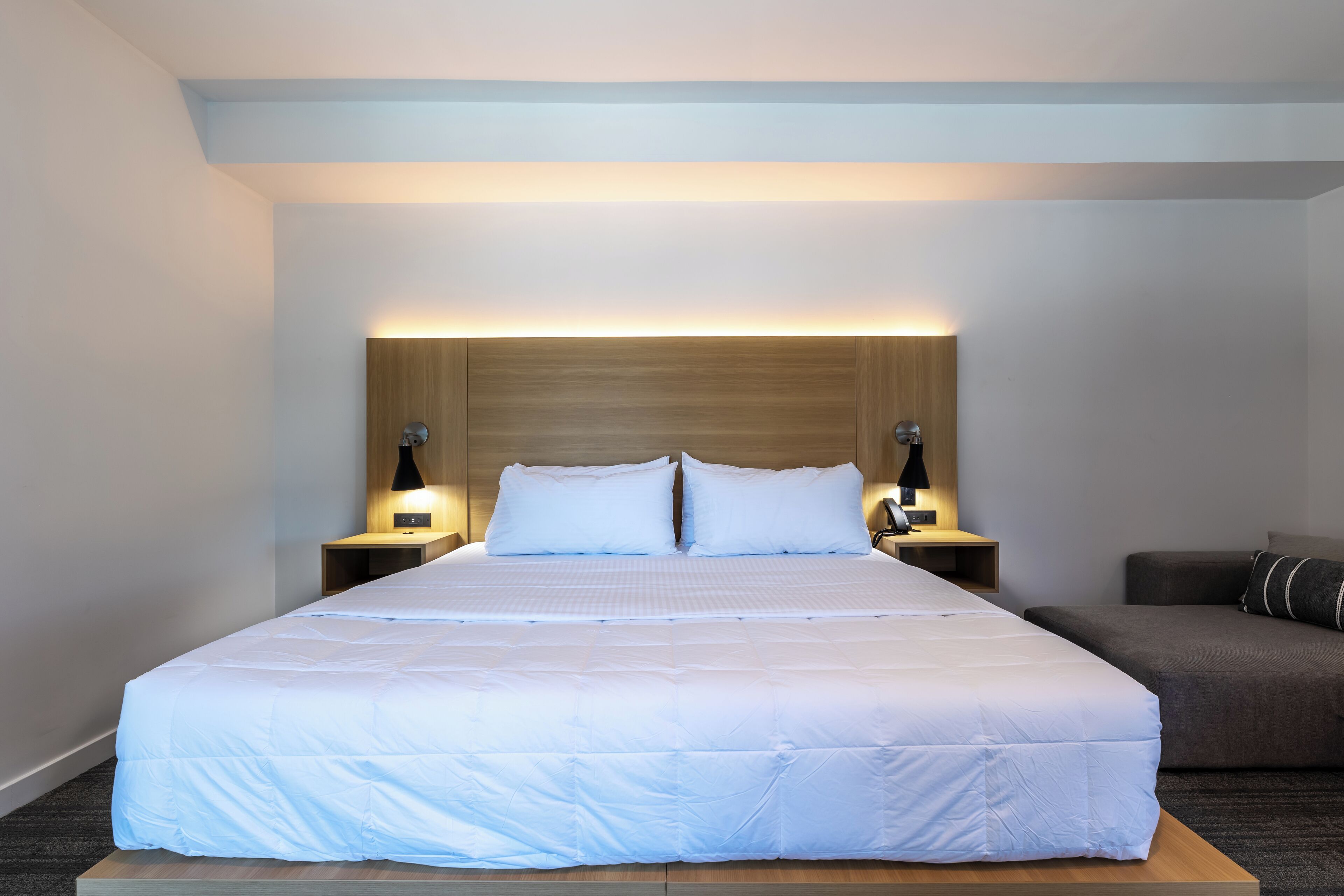 A large bed with white bedding, two bedside tables with lamps, and a dark-colored sofa.