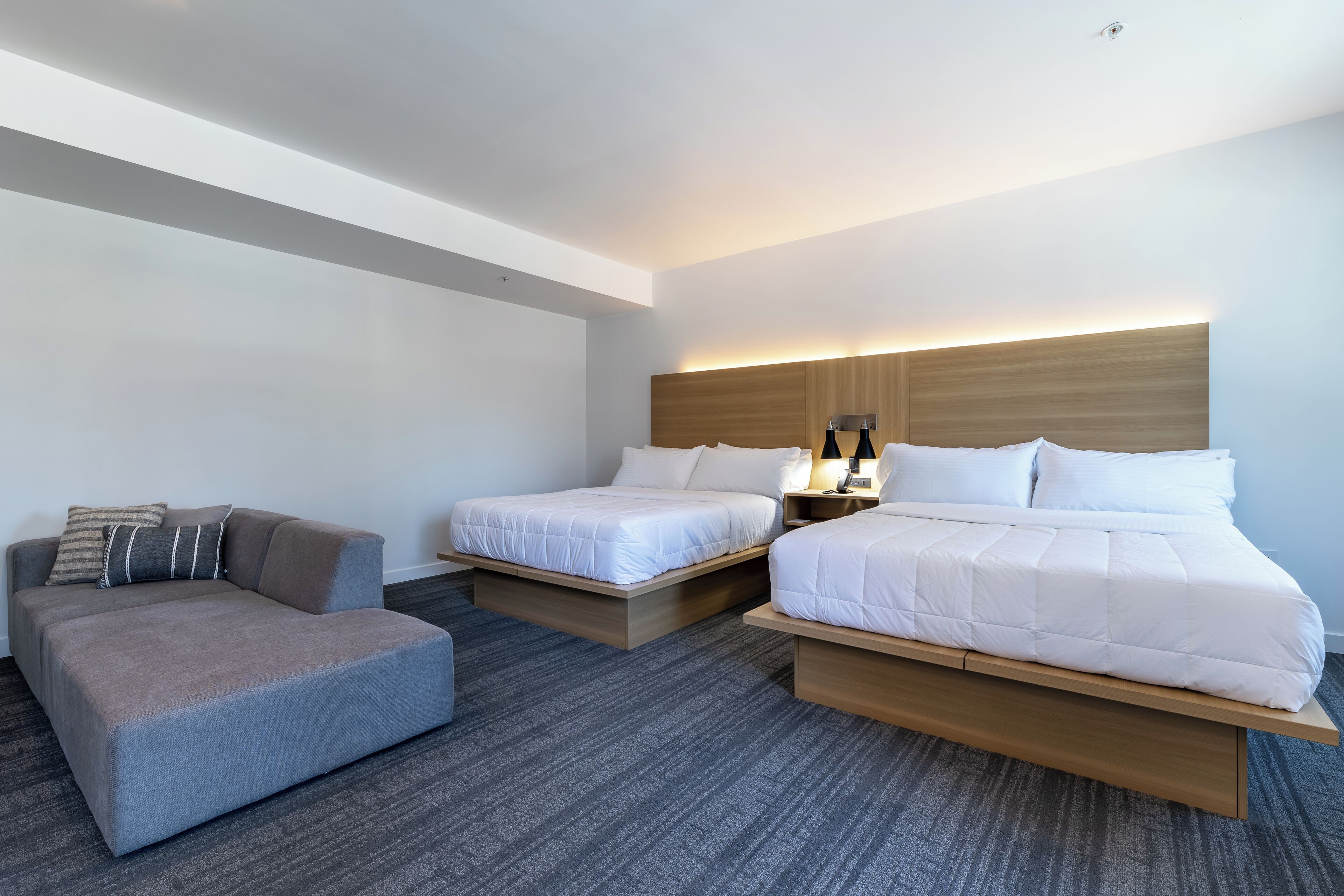Een moderne hotelkamer met twee bedden, een bank en een nachtkastje met lampen.