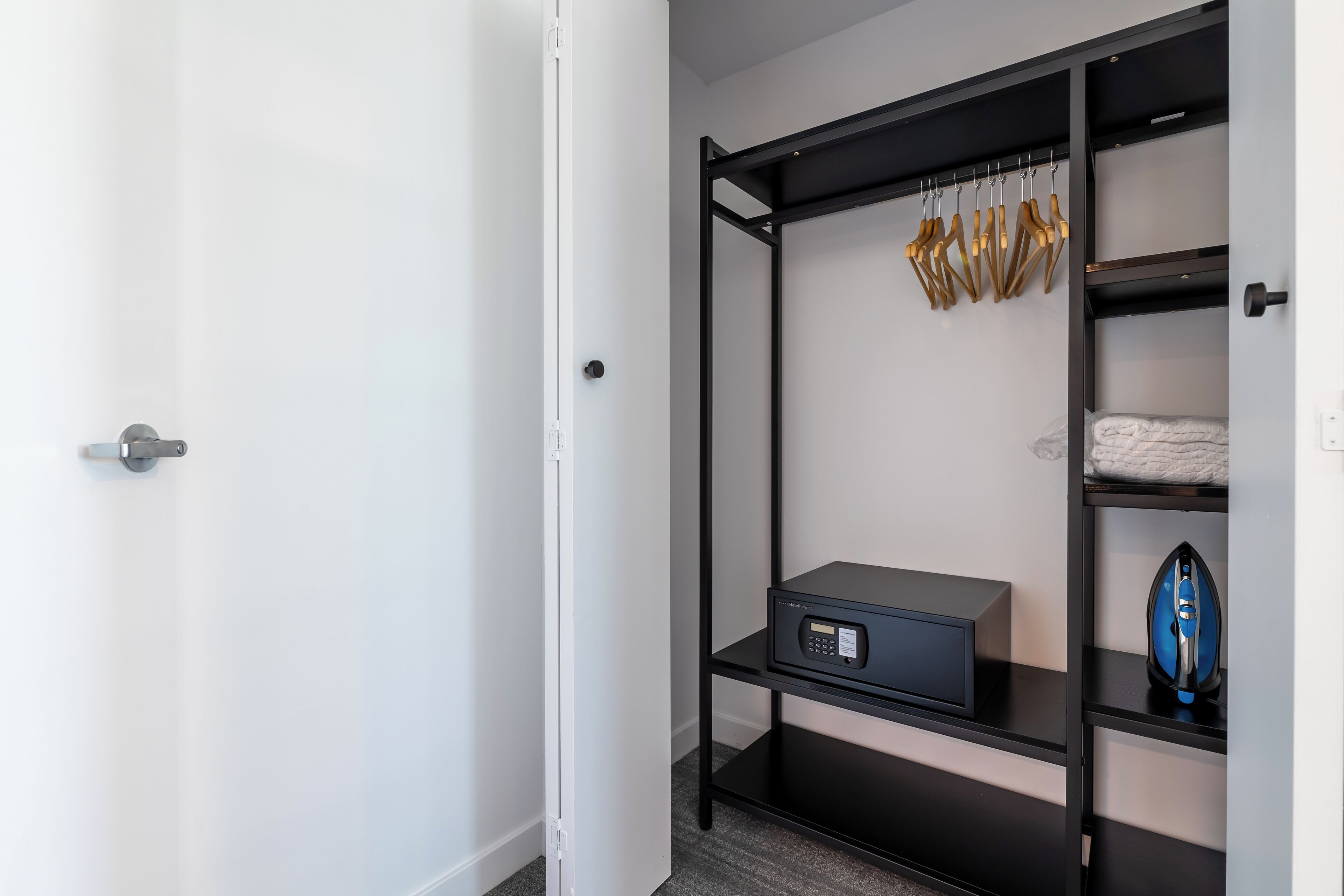 Une pièce comprenant une armoire en métal noir, un coffre-fort numérique et un fer à repasser bleu posé sur des étagères.