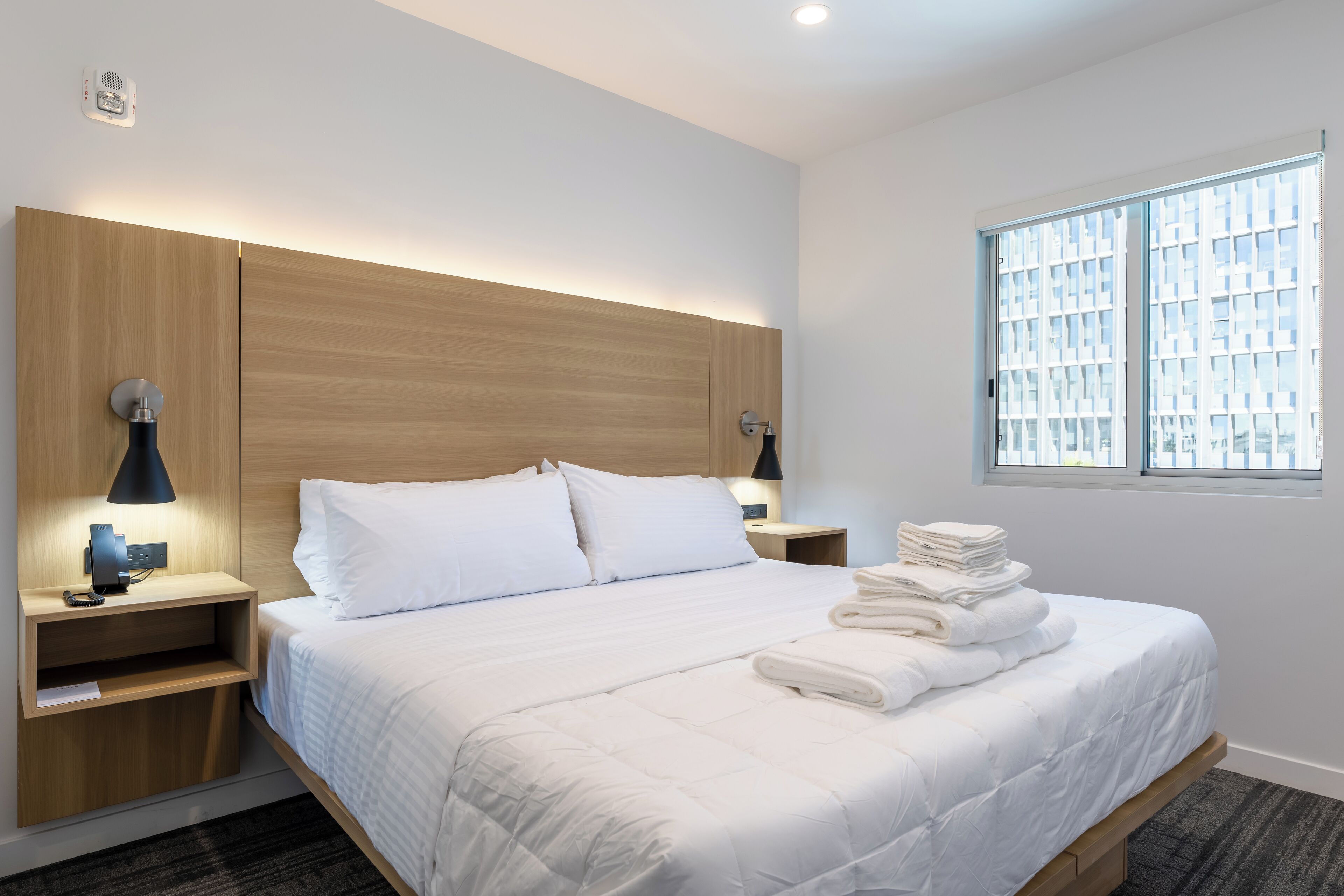 Une chambre d’hôtel moderne avec un grand lit, une tête de lit en bois, des lampes de chevet et une fenêtre donnant sur un beau paysage.