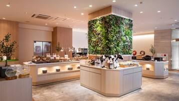A modern hotel lobby with a central reception desk, a vertical garden, and a seating area with tables.