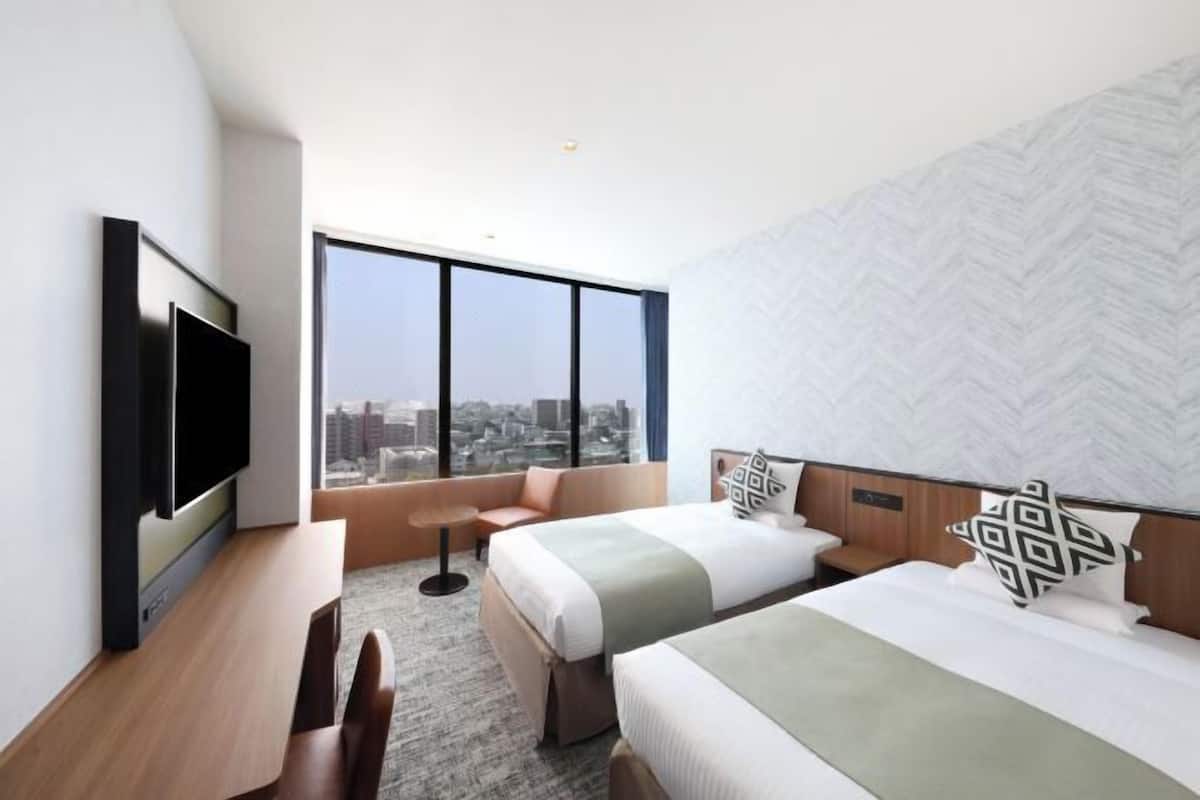 A hotel room with two beds, a TV, a city view, and a herringbone-patterned wall.
