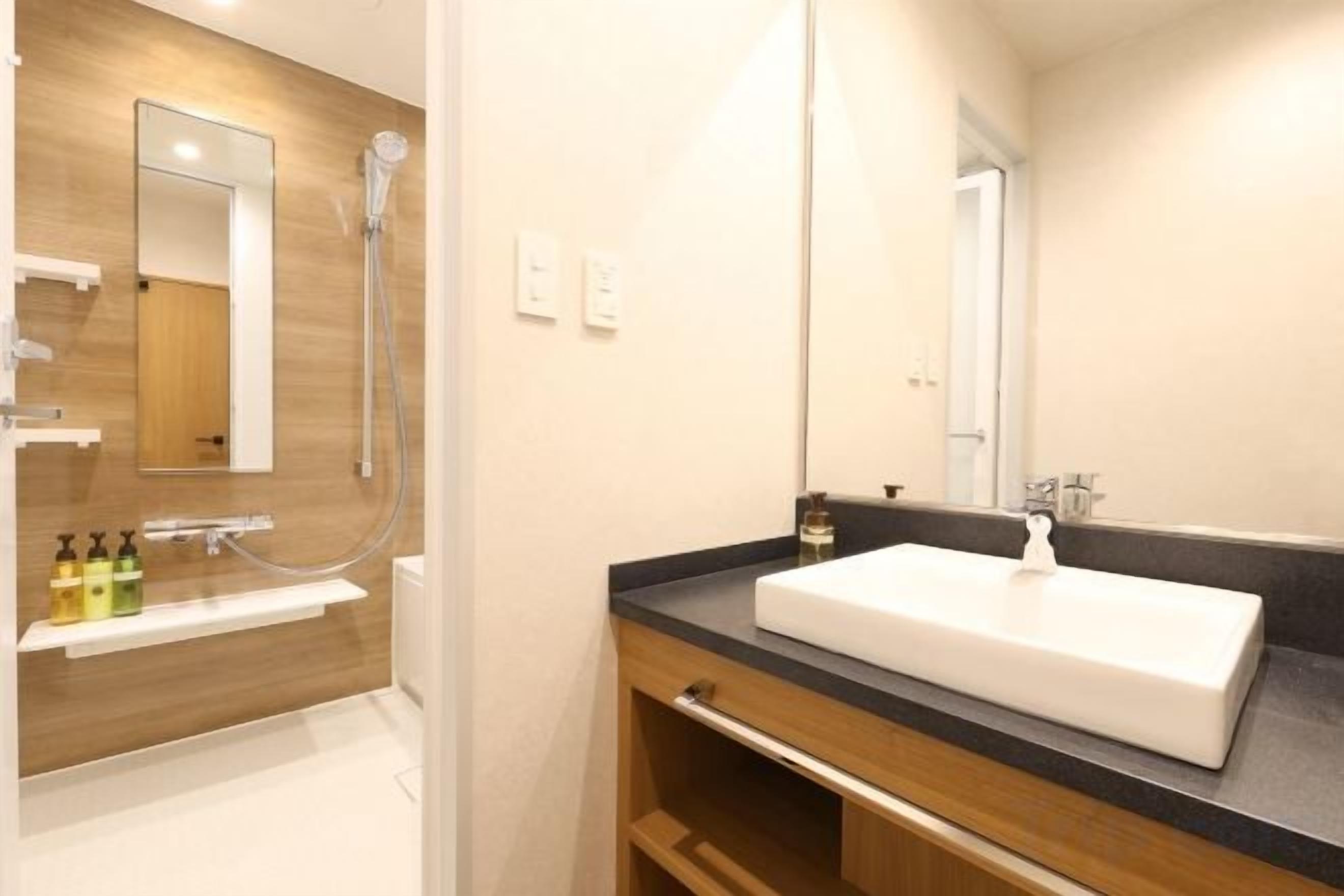 A modern bathroom with a wooden vanity, a white sink, and a large mirror.