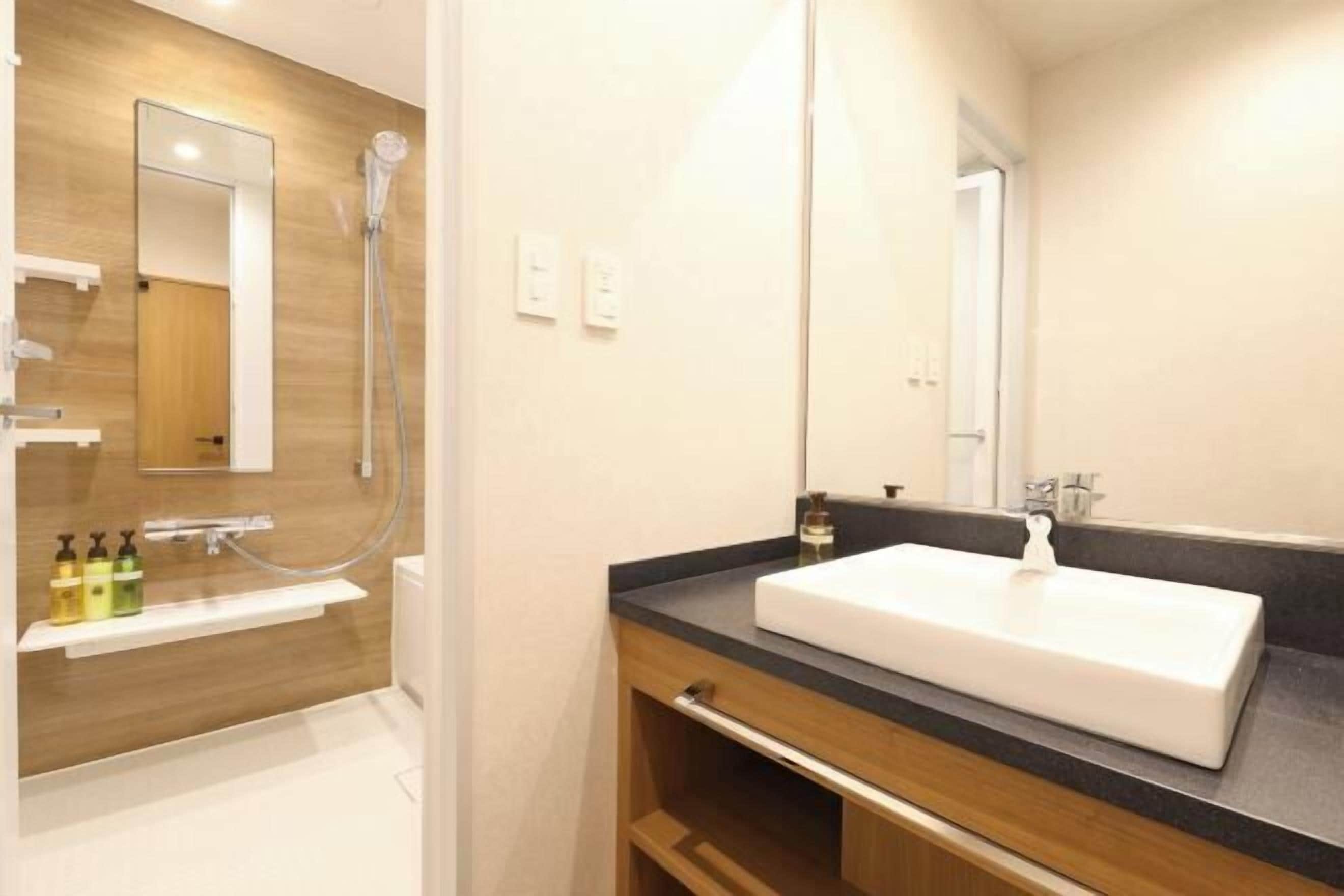Un baño moderno con tocador de madera, un lavabo blanco y un espejo grande.