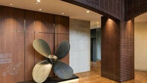 Un vestíbulo moderno con una gran escultura metálica de ventilador, paneles de madera y una columna de ladrillo.