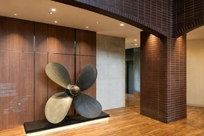 Un vestíbulo moderno con una gran escultura metálica de ventilador, paneles de madera y una columna de ladrillo.