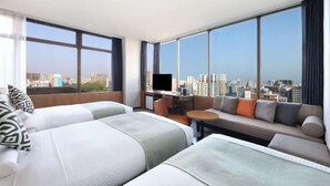 Habitación de hotel con dos camas, un sofá, televisión y vistas a la ciudad.