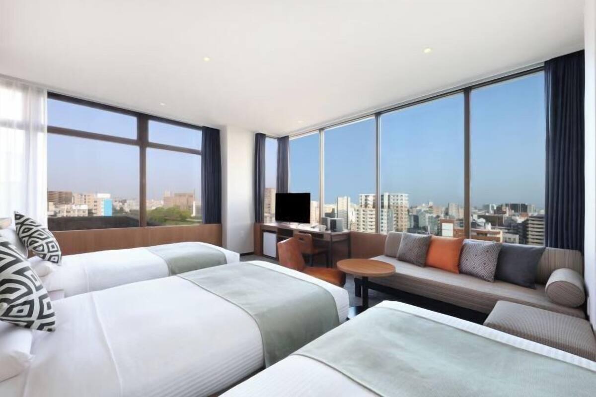 A hotel room with two beds, a sofa, a TV, and a city view.