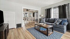 A modern living room with a grey sofa, wooden coffee table, and a TV stand. - Cozy, large home 5 blocks to downtown and island adventures and CP Pet friendly! (Port Clinton)