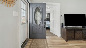 A hallway with a dark gray door, a wooden wall decoration, a large flat-screen TV, and a wooden cabinet. - Cozy, large home 5 blocks to downtown and island adventures and CP Pet friendly! (Port Clinton)