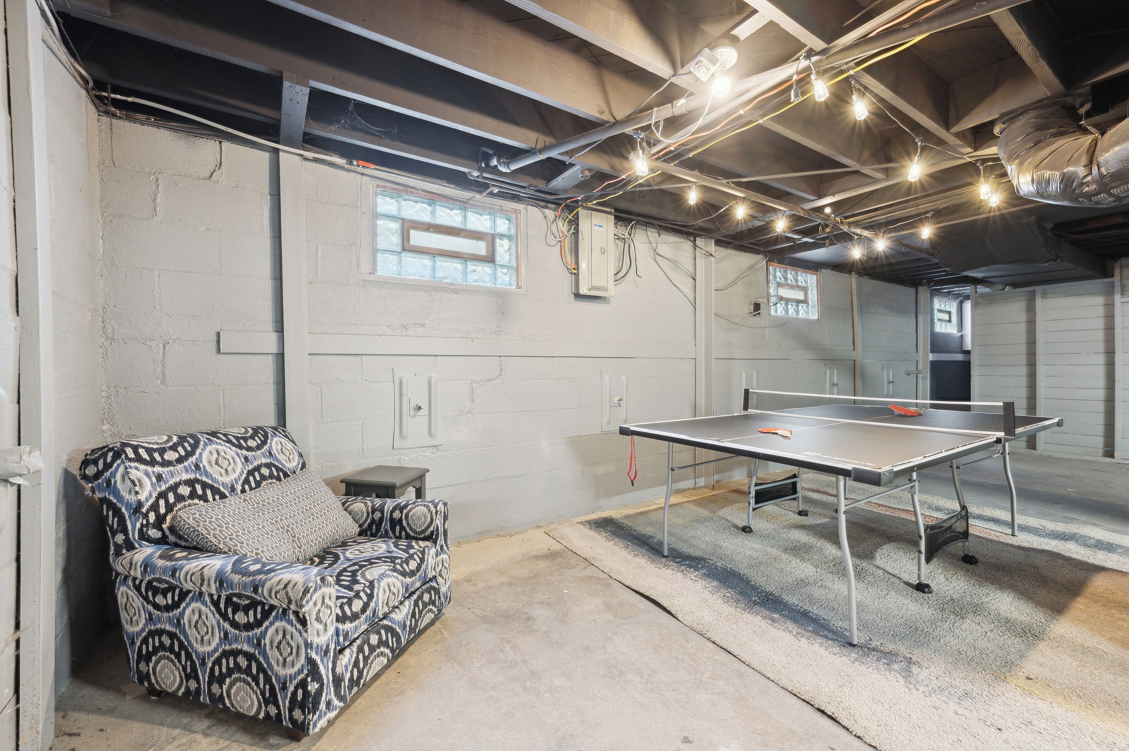 A room with a ping pong table, a patterned sofa, and a window with blinds.