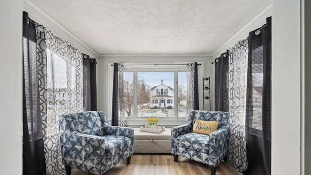 A room with two patterned armchairs, a small table with flowers, and a view of a house through large windows. - Cozy, large home 5 blocks to downtown and island adventures and CP Pet friendly! (Port Clinton)